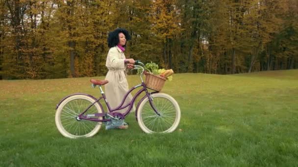 美しいアフリカの女性は 緑の芝生に緑のバスケットが付いているレディースバイクで散歩し 美しい風景を眺め 新鮮な空気を呼吸します 高品質の4K映像 — ストック動画