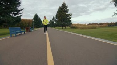 Sarı güneş gözlüklü, uzun boylu, zayıf bir adam neon yeşil spor ceket giyiyor, siyah pantolon güzel bir parkta bisiklet yolunda güzel bir günde hızla koşuyor. Yüksek kalite 4k görüntü