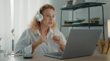 İnternetteki konferans sırasında masada oturan orta yaşlı, kulaklık takan hoş bir sarışın. Çevrimiçi eğitim veren profesyonel bir kadın. Yüksek kalite 4k görüntü