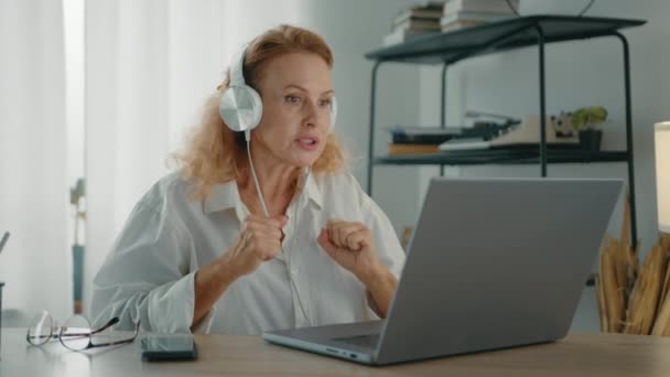 素敵な中年のブロンドは ラップトップを使用して ノートパソコンを使用して 自宅でテーブルに座っています オンライントレーニングを行う女性プロフェッショナル 高品質の4K映像 — ストック動画