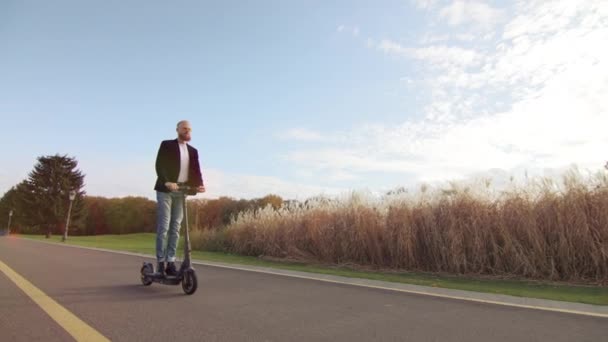 低角度的年轻男性 留着红胡子 戴着太阳镜骑着电动车 观察大自然的美丽 荒废的公园 绿绿的草坪 高质量的4K镜头 — 图库视频影像