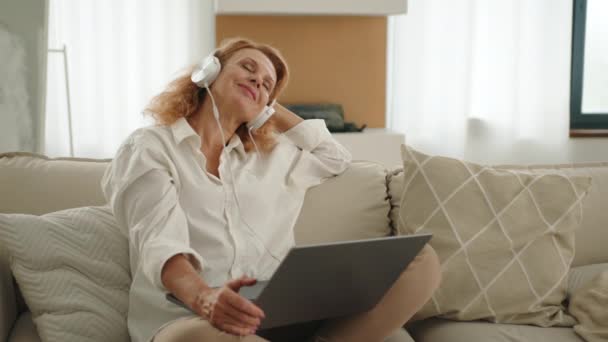 Smiling Relaxed Woman Wearing Headphones Sitting Modern Sofa Light Spacious — Stock Video