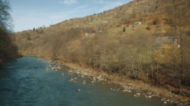 Sonbahar ağaçları ve çimenleriyle dağın eteklerinden akan sakin mavi bir nehrin kırsal manzarası. Dağlarda huzurlu bir hayat. Yüksek kalite 4k görüntü