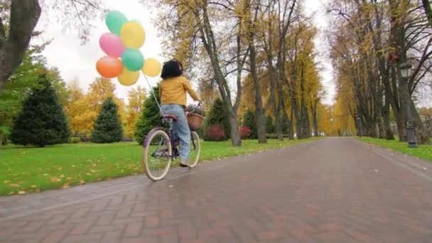 穿着红色耳机骑在复古自行车上的有色女人 在自行车座椅上绑着彩色气球 秋天的美丽 高质量的4K镜头 — 图库视频影像