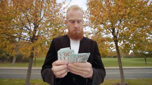 砂漠の秋の公園に一人で立っている黒いジャケットの若い赤身の男は 現金を数えることに焦点を当てて 大きなドルを手に持っていました 運が良かった 高品質の4K映像 — ストック動画