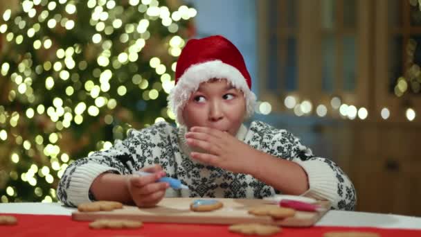 Dzieciak Swetrze Ozdobą Zimową Siedzi Świątecznie Urządzonej Kuchni Maluje Piernikowego — Wideo stockowe