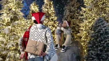 9-10 yıllık gülümseyen çocuk muhteşem kış mevsiminde kar yağışı ve ışıklandırılmış Noel ağaçlarıyla otururken Afrikalı kadın, annesi Noel hediyesi veriyor. Yüksek kalite 4k görüntü