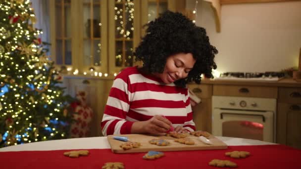 黑人女人沉迷于在装饰华丽的厨房里粉刷姜饼男 小孩躲在桌子底下 偷偷地拿着饼干 高质量的4K镜头 — 图库视频影像