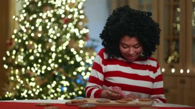 Koyu tenli kıvırcık kadın oğlunun gizlice masadan kurabiye aldığını fark etmeden zencefilli kurabiye süslemeye daldı. Noel havası. Yüksek kalite 4k görüntü