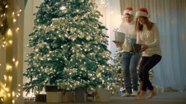 Genç çift Noel ağacının altına hediye koydu. Erkek ve kadın yeni yıl arifesinde hediye kutuları saklarlar. Yüksek kalite 4k görüntü