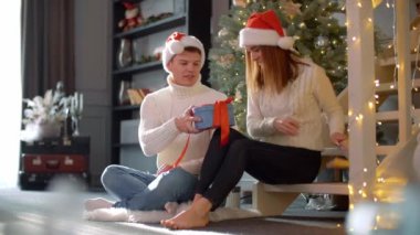 Adam sevgilisine Noel hediyesi veriyor. Kadın hediyeyi açar ve erkek arkadaşını öper. Yüksek kalite 4k görüntü