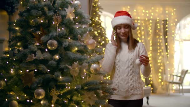 年轻的高加索女人在装饰圣诞树的时候有一个电话交谈 快乐的女孩把圣诞球放在了传统的树上 高质量的4K镜头 — 图库视频影像