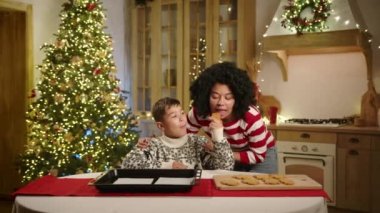 Mutlu anne ve küçük oğlu, mutlu bir şekilde dekore edilmiş mutfakta Noel ağacıyla süslenmiş çelenk, zencefilli ekmek yapan adamlar, ev yapımı fırın örnekleri alıp sarılıyorlar. Yüksek kalite 4k görüntü