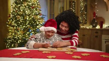 Noel Baba şapkalı mutlu anne ve çocuk Noel arifesini mutfakta ev yapımı zencefilli kurabiyeleri güzel süslenmiş Noel ağacıyla boyayarak geçiriyor. Yüksek kalite 4k görüntü