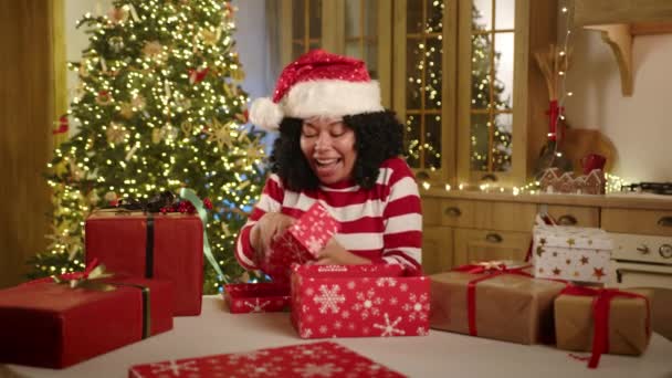身穿圣诞装束的漂亮黑人女人打开礼品盒 在现代化的厨房里欢声笑语 装饰着圣诞装饰品 又大又明亮的圣诞树 高质量的4K镜头 — 图库视频影像