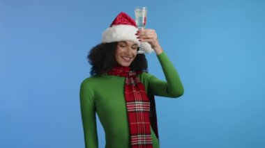 Yeşil kazak giyen neşeli, kırmızı uzun kareli atkı boynundaki şampanya kadehiyle baştan çıkarıcı bir şekilde kameraya poz veriyor, şerefe. Xmas ruhu. Yüksek kalite 4k görüntü
