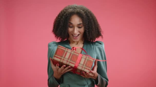 非常快乐可爱的女人摆出圣诞礼物的姿势 用红色的格子纸包着 红色的背景与之隔离 女士做鬼脸 高兴得发抖 高质量的4K镜头 — 图库视频影像