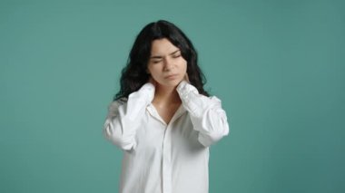 Kız, gerilimi azaltmak için elleriyle boynunu ovuyor. O, mavi arka plana karşı beyaz bir gömlek giyiyor. Yüksek kalite 4k görüntü