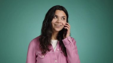 Güzel genç esmer kız cep telefonuyla konuşuyor. O, mavi bir arka planda pembe elbiseler içinde duruyor. Yüksek kalite 4k görüntü