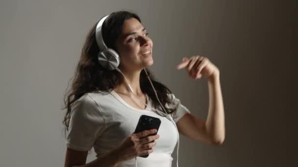 Dziewczyna Tańczy Białymi Słuchawkami Telefonem Rękach Jest Białej Koszulce Wysokiej — Wideo stockowe