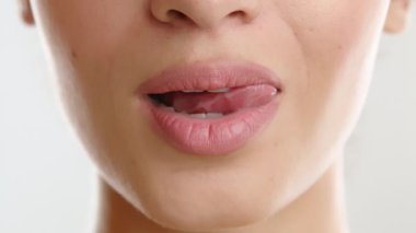 Hassas yüz hatları olan zayıf bir kadının yüzünün alt kısmını kapatın. Doğal renkte ruj, beyaz dişler boyunca baştan çıkarıcı bir dil. Yüksek kalite 4k görüntü