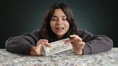 Bir kız parasının üzerine yatar ve gösterişli bir şekilde yüz dolarlık banknotlardan birini yırtar, böylece çok parası olduğunu gösterir. Yüksek kalite 4k görüntü