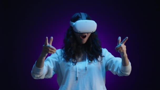 一个戴着虚拟现实眼镜的黑发女人拿着一个虚拟武器 在玩游戏 她住的房间背景是深紫色的 蓝光照亮着她 高质量的4K镜头 — 图库视频影像