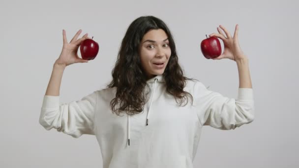 아름다운 소녀가 사과를 보여주고 있습니다 그녀는 배경에 후드에 소녀는 행복하고 — 비디오