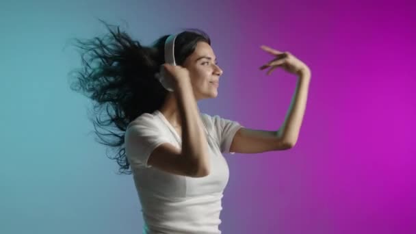 ヘッドフォンで踊るハッピーガール 風は彼女の髪を通して吹く 彼女は青いピンクの背景にいる 高品質の4K映像 — ストック動画