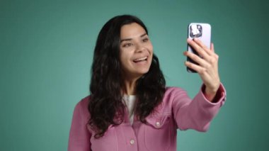 Mutlu kız cep telefonuyla bir video görüşmesi yapıyor. O, mavi bir arka planda pembe giyinmiş. Yüksek kalite 4k görüntü