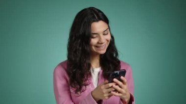 Güzel kız telefonuna bir mesaj yazmaya odaklanmış durumda. O, mavi bir arka planda pembe giyinmiş. Yüksek kalite 4k görüntü