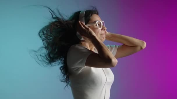 戴耳机的女孩没有抑制住自己的情绪 高兴地尖叫着 风吹乱了她的头发 她站在蓝色粉红的背景上 高质量的4K镜头 — 图库视频影像