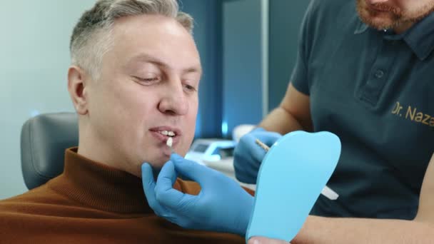 中位男性患者的照片 向医生展示两排牙齿 戴手套照镜子 在扶手椅上选择合适的牙科植入物 高质量的4K镜头 — 图库视频影像