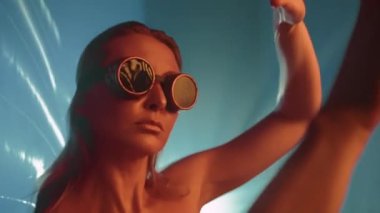 Siber punk gözlükleriyle altın ten rengine sahip bir model, projektörün arkasındaki ışığın geçtiği bir film arasında dans eder. Yüksek kalite 4k görüntü