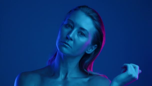 裸で撃たれた女の子は スムーズに動き カメラに直接見える 肌はかっこいい青い色をしている 青とピンクの光線が顔に当たっている スローモーション 高品質の4K映像 — ストック動画