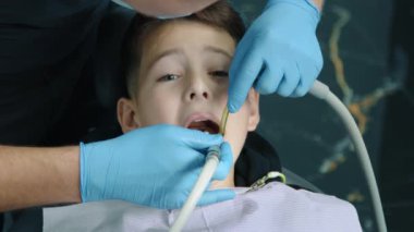 9-10 yıllık cesur bir hastanın dişçi koltuğunda ağzı sonuna kadar açık otururken erkek doktorun diş türbinini su püskürterek kullanmasına yakın çekim. Hijyen. Yüksek kalite 4k görüntü