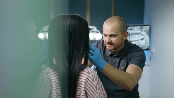 在牙科诊所做完牙科诊所会诊后拍到的黑发女士肩膀以上的照片 戴乳胶手套的牙科医生看着病人的牙齿 高质量的4K镜头 — 图库视频影像