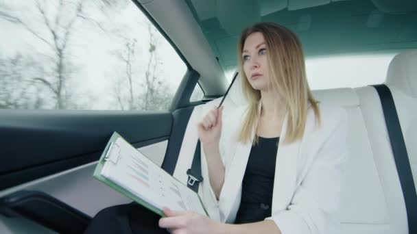 女の子は車の後部座席のチャートに注意深く取り組んでおり 彼女の仕事に大きな焦点と集中を示しています 高品質の4K映像 — ストック動画