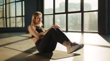 Yan kıvrımlarla çalış. Ellerinde topla karın egzersizi yapan bir kız. O, sıcak güneş ışığında. Spor ve spor. Eğitim, eğitim ve sağlık kavramı. Yüksek kalite 4k görüntü.