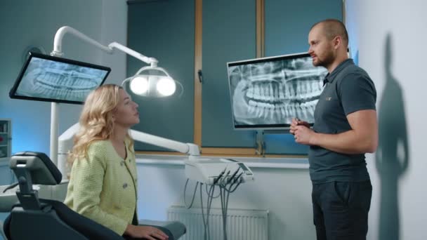 Bonito Jovem Atlético Dentista Masculino Respondendo Perguntas Para Bela Paciente — Vídeo de Stock
