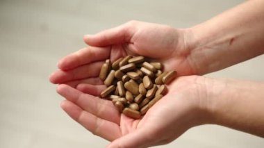 Çerçevede avuçlar beliriyor, ellerinde bir sürü koyu renkli ilaç var. Kız doğal bitkilerden yapılmış çok sayıda tablet gösteriyor. İlaç ve sağlık. Sağlık ve güzellik. 4k görüntü.