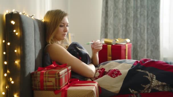 クリスマスの日に病気になった孤独な少女は 体温を測るベッドに座った 贈り物に囲まれて 彼女は幸せではない 彼女は咳をして 気分が悪くなった 高品質の4K映像 — ストック動画