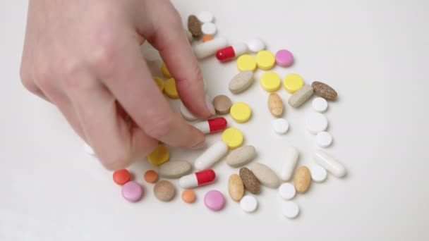 不同形状和颜色的各种药丸散布在一张白桌子上 一只手选择一种药丸 象征着在药物和医疗保健方面的选择 — 图库视频影像
