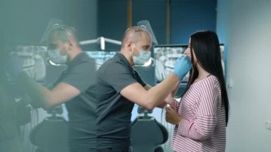 Erkek dişçi, dişlerini iyi donanımlı bir dişçi muayenehanesinde duran bir kadının doğal dişlerine yerleştiriyor. Kozmetik dişçilik, beyazlatma. Yüksek kalite 4k görüntü