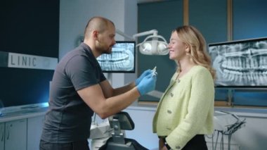 Tam teçhizatlı bir ofiste genç bayan hastaya farklı diş implantlarını denerken ortodontist. Yüksek kalite 4k görüntü