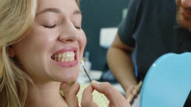Sağlıklı, parlak ciltli, dişlerine bakan hoş bir kadın. Erkek doktor diş implantı örneği uyguluyor. Hafif donanımlı dişçi ofisi. Yüksek kalite 4k görüntü