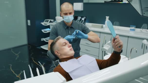 中年男性の歯の状態をチェックする歯科スクレーパーとミラーを使用した医療用手袋の男性歯科医 口の広い開いたホールディングミラーを持つ患者 高品質の4K映像 — ストック動画