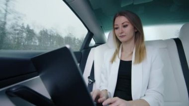 Lüks bir arabanın arka koltuğunda dizüstü bilgisayarda çalışan, beyaz ceketli, iş ve finans sektöründe faaliyet gösteren yalnız bir kadın. Yüksek kalite 4k görüntü.