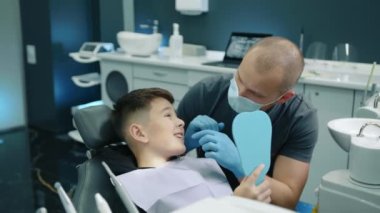 Diş ağrısı çeken genç bir hasta ağzını kocaman açıyor, diş sorunu gösteriyor, tıbbi maske takan profesyonel bir dişçi ve çocuğun ağız boşluğunu muayene eden eldivenler. Yüksek kalite 4k görüntü