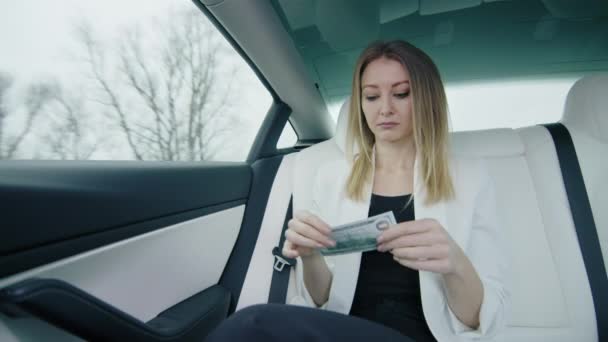 仕事車の後部座席にいる女性は 100ドルの請求書を涙を流し 悲しいことに窓の外を見ます 外の暗い天気は彼女の気分と一致する 高品質の4K映像 — ストック動画